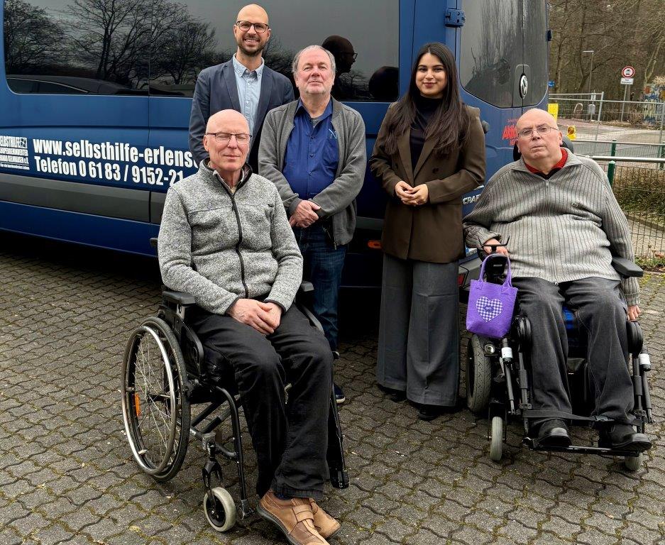 Abgebildet sind vier Vertreter der Selbsthilfe Körperbehinderter Main-Kinzig e.V. (SHK) und Mahwish Iftikhar. Die Person links und die Person rechts auf dem Bild sitzen im Rollstuhl. Hinter den Menschen parkt ein Bus der Selbsthilfe.